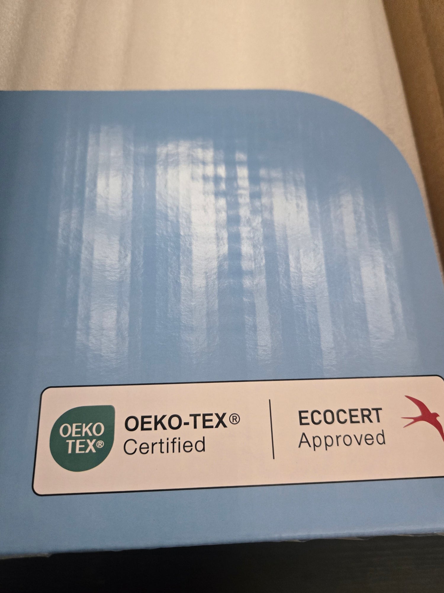 A close-up of a blue fabric sample or swatch card with rounded corners, featuring an OEKO-TEX and ECOCERT certification label at the bottom.